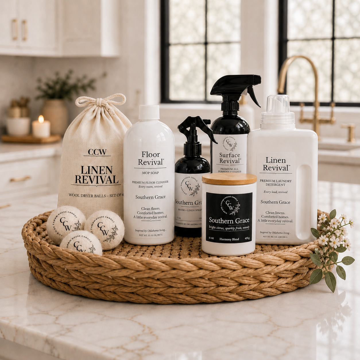 CCW Home Revival Set featuring Southern Grace scented laundry detergent, mop soap, room and linen spray, Surface Revival all-purpose cleaner, wool dryer balls, and candle displayed on a woven tray in a bright farmhouse kitchen.